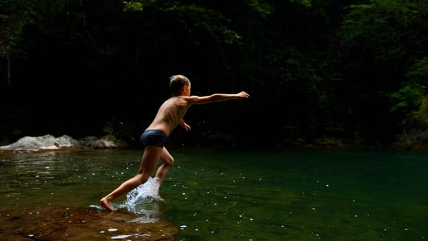 Boy child jumping in cold mountain river on a summer day. Creative. Hiking in summer jungles