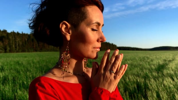 Young pretty girl woman meditating with closed eyes. Stock clip. Praying while standing in a field with a beautiful view on a windy summer day at sunset