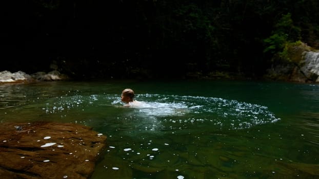 A young boy bathing in a mountain river pool. Creative. Child having fun in a summer natural pond