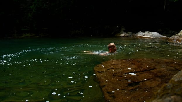 Slow motion of a boy jumping into a waterfall and natural pond. Creative. Young boy child having fun in jungles