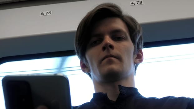 Caucasian man looking down on phone and looking stressed. Stock clip. Face of a man sitting near the window in the tram or bus