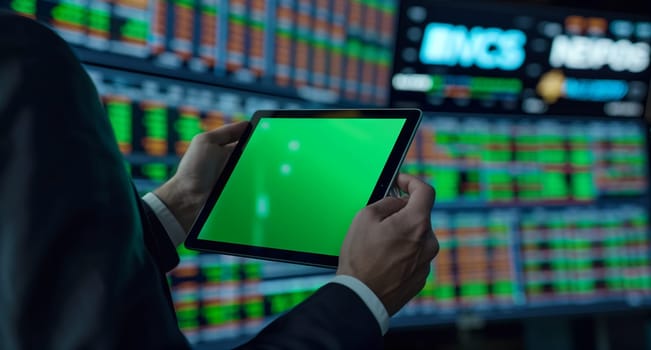 A man is gesturing while holding an electronic device with a green screen. The display device is likely a tablet used for recreation, games, and multimedia purposes