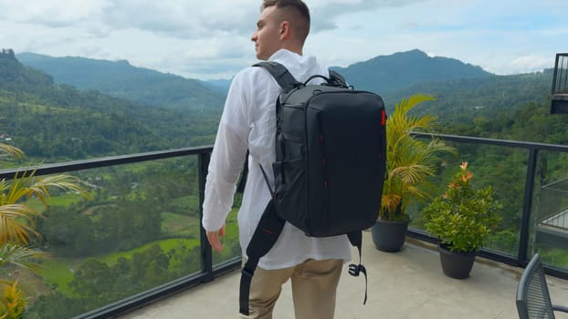 Man with view of tropical mountain valley. Action. Man on observation deck in tropical mountains. Man with backpack on sightseeing attraction overlooking green mountains.