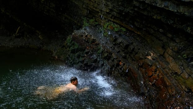 Child boy swimming in mountain pond with waterfall. Creative. Child on summertime vacation refreshing in river