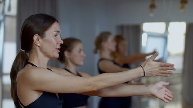 Group of sportive people during a gym training with a coach. Media. Girls group of athletes swinging hands before starting a workout yoga session