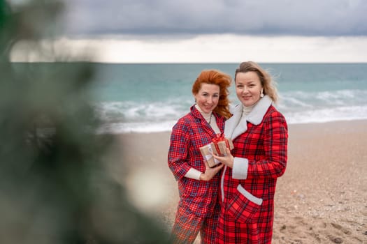 Sea two Lady in plaid shirt with a christmas tree in her hands enjoys beach. Coastal area. Christmas, New Year holidays concep.