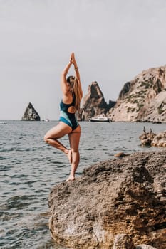 Yoga on the beach. A happy woman meditating in a yoga pose on the beach, surrounded by the ocean and rock mountains, promoting a healthy lifestyle outdoors in nature, and inspiring fitness concept