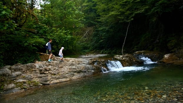 Woman and boy walking along natural pond with small waterfall, summer time. Creative. Travelling in jungles