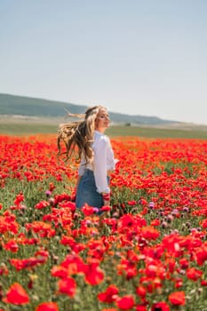 Happy woman in a poppy field in a white shirt and denim skirt with a wreath of poppies on her head posing and enjoying the poppy field