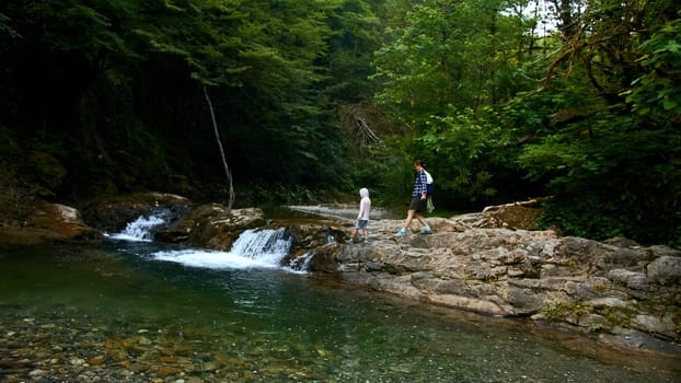 Woman and boy walking along natural pond with small waterfall, summer time. Creative. Travelling in jungles