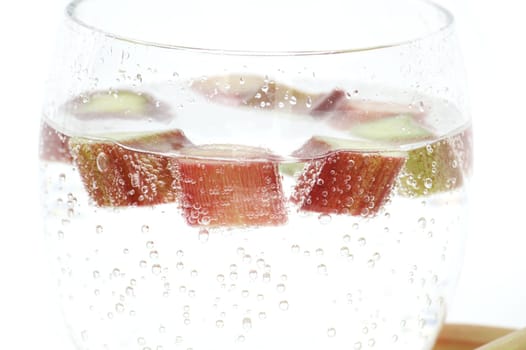 Transparent glass filled with cold water and several pieces of rhubarb isolated on white background