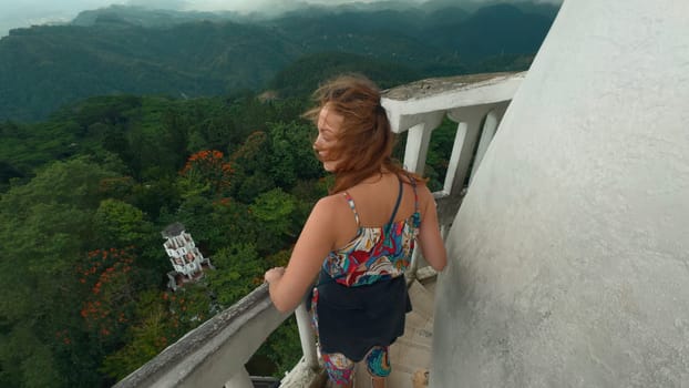 Woman on historic tower in mountains. Action. Beautiful woman on observation deck of ancient tower. Tourist attraction at top of historic tower in green mountains.