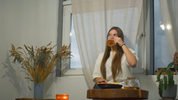 Young woman romantically drinks tea in cafe. Media. Young female student is relaxing in cafe with tea. Beautiful young woman is drinking tea alone in cozy cafe.