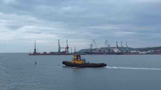 Fishing boat on background of port in cloudy weather. Clip. Fishing vessel sails out of seaport into sea. Fishing boat sails into sea on cloudy day.