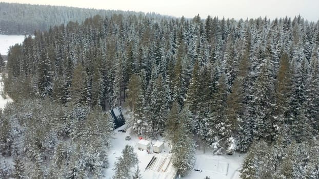 Aerial of magic snowy winter wonderland with a small glamping unbuilt house among trees. Clip. Winter season in snowy mountain forest