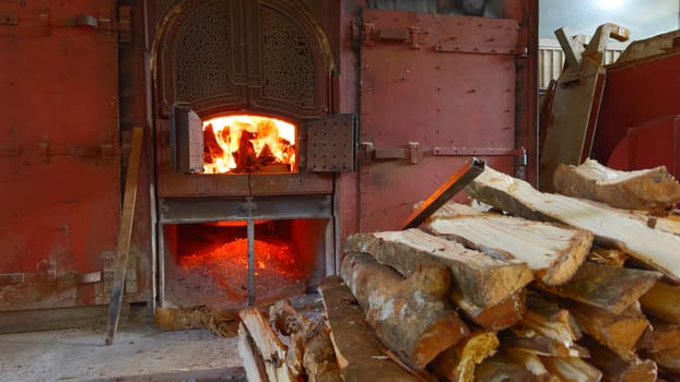 Old stove with firewood in summer. Action. Beautiful oven doors in wall with fire. Outdoor stove with burning wood inside on summer day.