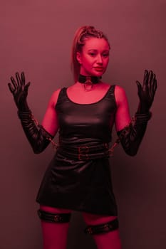 Beautiful young woman in a leather dress and bondage set posing on red light backgound