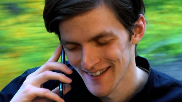 Caucasian man smiling with eyes closed while talking with somebody on the smartphone. Stock clip. Face of a man sitting near the window in the tram or bus