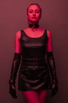 Beautiful young woman in a leather dress and bondage set posing on red light backgound