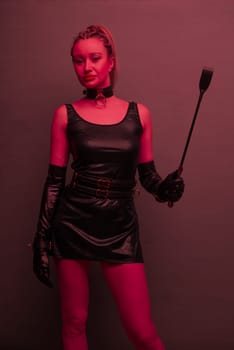 Beautiful dominant brunette mistress woman in latex dress and gloves posing with riding crop on red light backgound