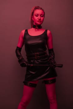 Beautiful dominant brunette mistress woman in latex dress and gloves posing with riding crop on red light backgound