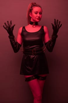 Beautiful young woman in a leather dress and bondage set posing on red light backgound