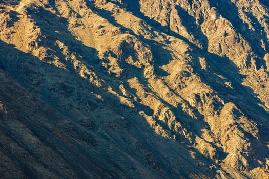 Natural landscape featuring a close up full-frame telephoto view of a mountain side slope under direct evening sun light.