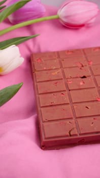 A bar of pink ruby chocolate with sublimated freeze-dried strawberries and almonds and spring tulip flowers . A dessert based on berries and nuts for International Women's Day, March 8, mother's day