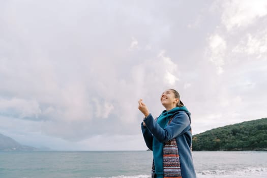 Young woman is standing by the sea with a kite spool in her hands, straightening the thread, and looking up. High quality photo