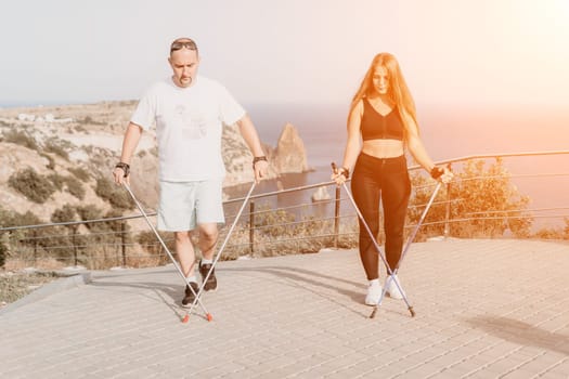 Happy Middle aged couple or friends practicing nordic walking in park near sea. Mature couple with trekking poles walking, practicing Nordic walking outdoors. Aging youthfully and sport concept.