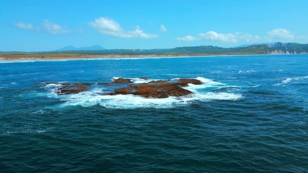 Aerial picturesque seascape with blue water, boulders rising up above sea surface. Clip. Summer coastline and blue sky above