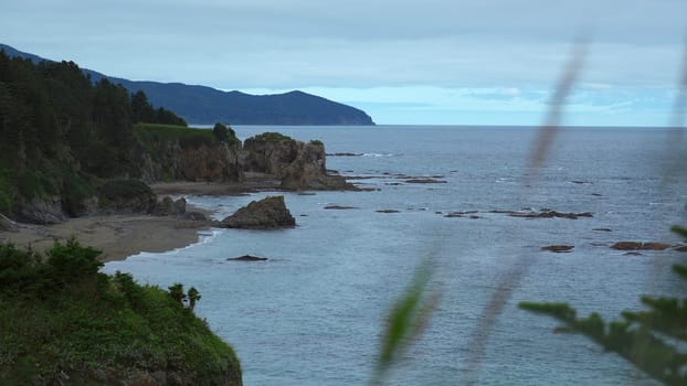 Beautiful rocky coast with greenery in cloudy weather. Clip. Top view of picturesque landscape of southern sea coast with rocks. Green rocky coast on cloudy day.