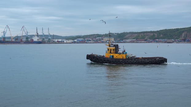 Fishing boat on background of port in cloudy weather. Clip. Fishing vessel sails out of seaport into sea. Fishing boat sails into sea on cloudy day.