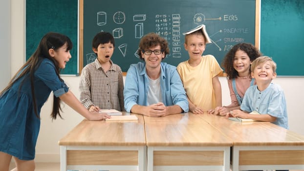Professional caucasian teacher and diverse student looking at camera while happy school boy smiling. Group of multicultural children smiling while standing in front of classroom. Education. Pedagogy.