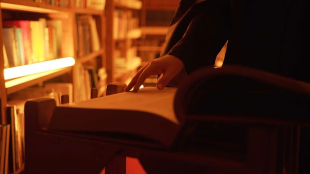 Close-up of mysterious man opening large book. Stock footage. Man opens book in dark library with flashing light. Secret society with mysterious books in night library.