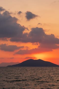 As the sun sets over the ocean, the sky transforms into a canvas of orange and red hues, casting a warm afterglow over the water and the distant mountain