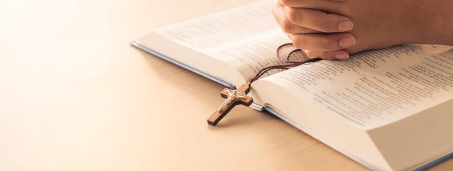 Asian male folded hand prayed on holy bible book while holding up a pendant crucifix. Spiritual, religion, faith, worship, christian and blessing of god concept. Blurring background. Burgeoning.