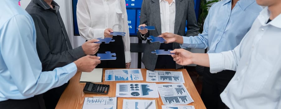 Corporate officer worker collaborate in office, connecting puzzle pieces with report paper on table as partnership and teamwork. Unity and synergy in business concept by merging jigsaw puzzle. Concord