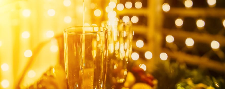 Two champagne glasses filled with champagne are placed on a table with a fruit arrangement. The glasses are surrounded by lights, creating a festive atmosphere. The table is set for a celebration or a special occasion