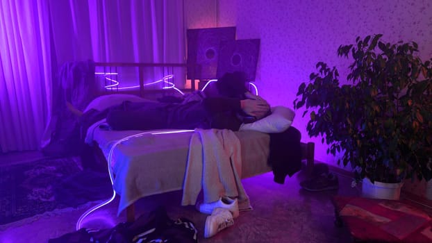 Man listening to music, using headphones in bedroom at night. Media. Man lying on his bed and enjoying music