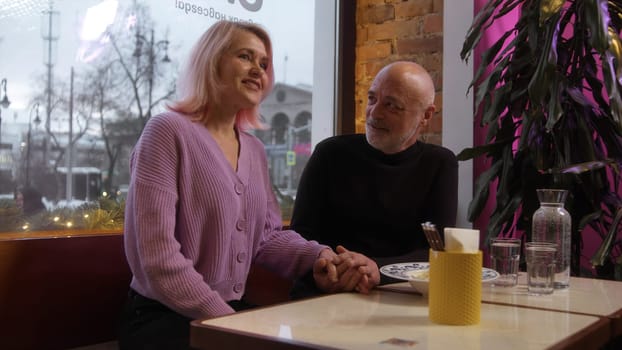 Beautiful elderly couple on date in cafe. Stock footage. Beautiful elderly couple is chatting on date. Stylish elderly couple chatting in cafe.