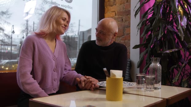 Beautiful elderly couple on date in cafe. Stock footage. Beautiful elderly couple is chatting on date. Stylish elderly couple chatting in cafe.