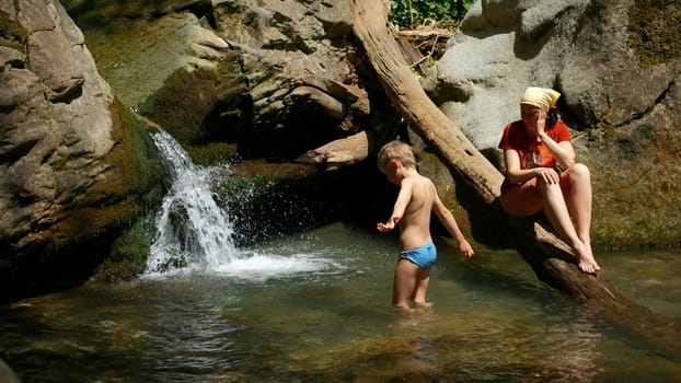 Mom with boy child in tropical waterfall. Creative. Family of hikers on a summer trip in jungles