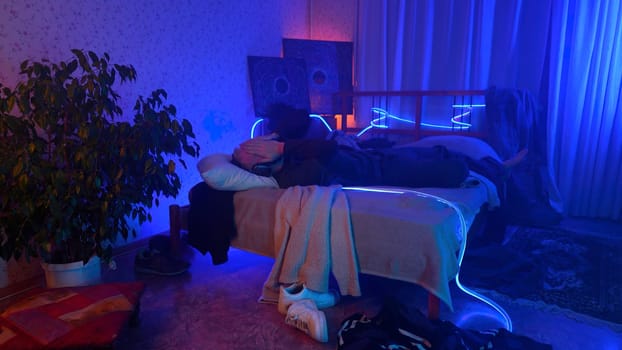 Man listening to music, using headphones in bedroom at night. Media. Man lying on his bed and enjoying music