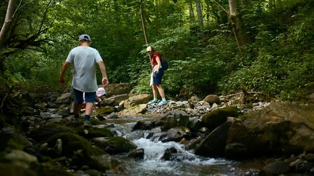 Family of mother and two boys jumping rocks across creek. Creative. Young travelers hiking together in North Carolina woods