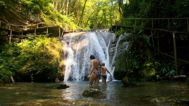 Woman and boy child bathing in beautiful waterfall in dense jungles. Creative. Woman and a boy in cold mountainous river