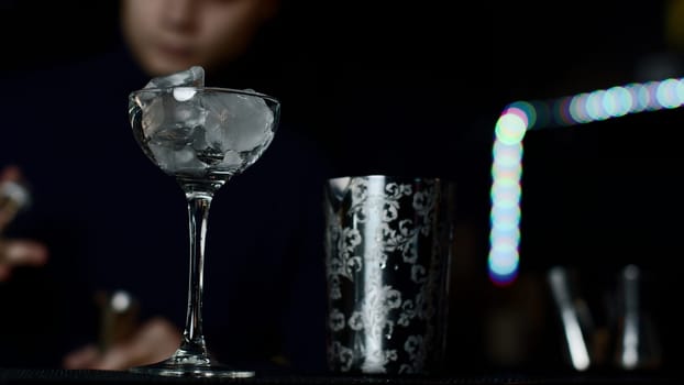 Close up of glass with ice cubes prepared for cocktail. Media. Bartender mixing alcohol liquids in a shaker