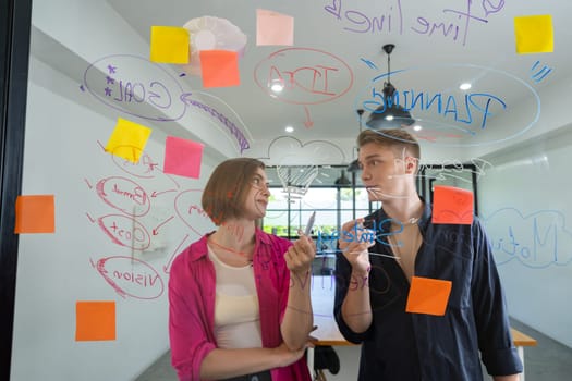 Couple of young creative start up business people brainstorming idea and solving problems by using sticky note and mind map at glass board, meeting room. discussing, working together. Immaculate.