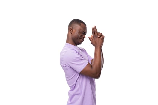 a young positive friendly American man with a short haircut is dressed in a lilac T-shirt standing sideways.