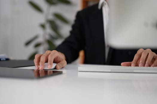 Cropped shot of businessman in black suit holding computer mouse working at desk.